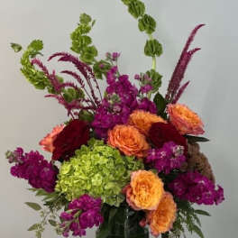 Tall mixed bouquet in a glass vase with orange, magenta, and green blooms
