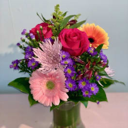 Mixed bouquet of pink roses, gerbera daisies, and purple daisies in a glass vase