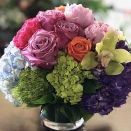 Colorful bouquet of roses, hydrangeas, and orchids in a glass vase