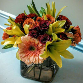 Bouquet of lilies, roses, and a gerbera daisy in a square glass vase