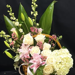 Basket arrangement of cream roses, pink lilies, and white hydrangea