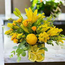 Yellow floral arrangement in a glass vase with lemons and citrus slices