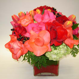Bouquet of red, pink, and coral roses in a square glass vase