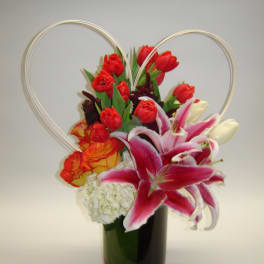 Red tulips and pink lilies in a dark vase with heart-shaped wire handles