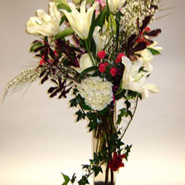 Tall bouquet of white lilies and mixed flowers in a clear glass vase