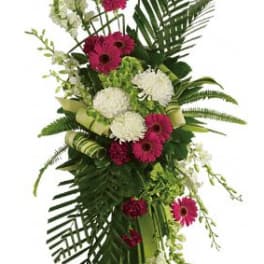 Tall arrangement of hot pink gerbera daisies, white mums, and orchids in a green glass vase