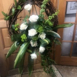 Standing grapevine wreath with white roses and green floral accents on a metal easel
