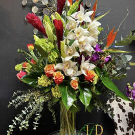Tall mixed bouquet with white orchids, orange roses, and red tropical blooms in a glass vase