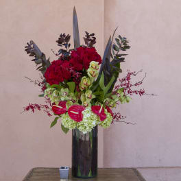 Tall arrangement of red roses, green orchids, and anthuriums in a dark vase