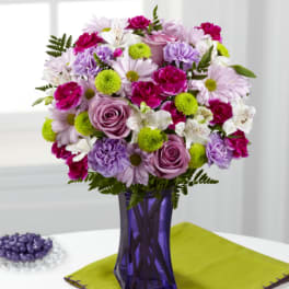 Mixed bouquet of pink, purple, and white flowers in a purple vase