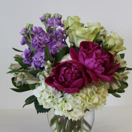 Mixed bouquet of white hydrangeas, purple stock, green roses, and magenta peonies in a glass vase