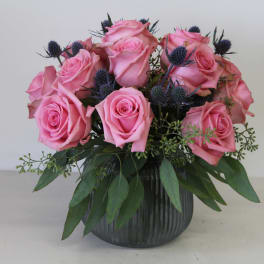 Pink roses arranged in a dark glass vase with blue thistle accents