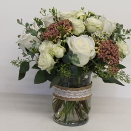 White roses and pink filler flowers in a glass vase with lace ribbon