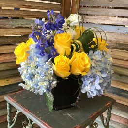 Yellow roses and blue hydrangeas in a black vase