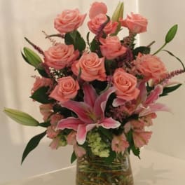 Arrangement of pink roses and lilies in a clear glass vase with a soft, romantic look