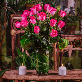 Pink roses arranged in a clear glass vase with candles on a wooden table