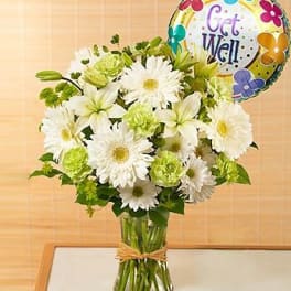 White daisy and lily bouquet in a glass vase with a Get Well balloon