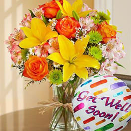 Bouquet of yellow lilies and orange roses in a glass vase with a "Get Well Soon" balloon