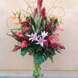 Tall tropical flower arrangement in a clear glass vase with pink lilies and bird of paradise