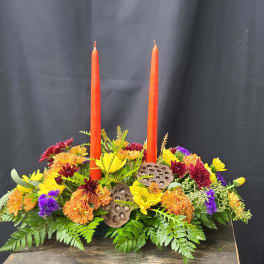Low floral centerpiece with two orange taper candles and mixed blooms