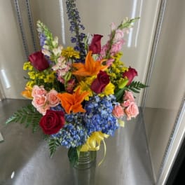 Mixed bouquet in a glass vase with roses, lilies, and blue hydrangeas