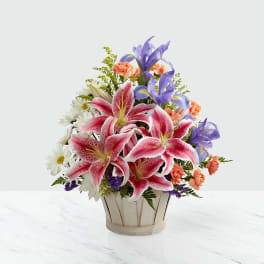 Basket arrangement of pink lilies, purple irises, and white daisies