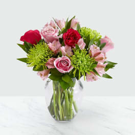 Pink and red roses with green chrysanthemums in a clear glass vase