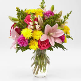 Mixed bouquet of pink lilies, roses, and yellow daisies in a glass vase