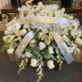 White funeral spray with ribbons reading Beloved Husband and Father