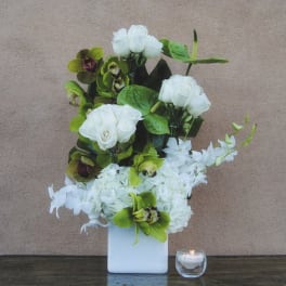 White floral arrangement in a square vase with a small candle beside it