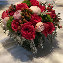 Compact arrangement of red roses and pale peonies in a low vase
