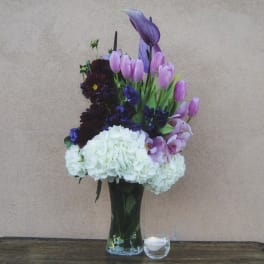 Tall bouquet of pink tulips, purple flowers, and white hydrangeas in a glass vase