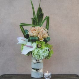 Tall floral arrangement with peach roses and white calla lilies in a wrapped vase