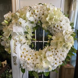 White funeral wreath with lilies, orchids, and daisies on a stand