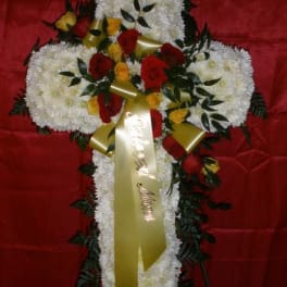 Cross-shaped floral tribute with white flowers, red roses, and gold ribbon