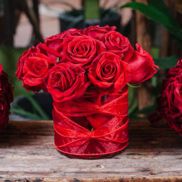 Red roses arranged in a glass vase wrapped with red ribbon