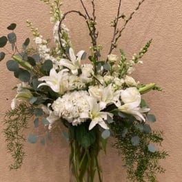 White lilies and hydrangeas in a clear glass vase with tall branches