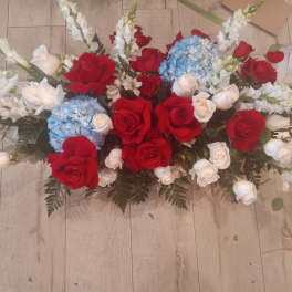 Casket spray with red and white roses, blue hydrangeas, and white lilies