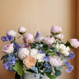 Pastel bouquet of roses, peonies, and blue flowers in a white vase