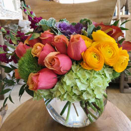 Mixed bouquet of roses, ranunculus, hydrangea, and calla lilies in a glass vase