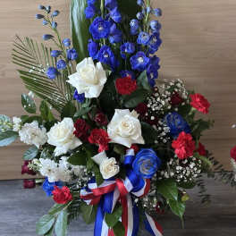 Tall red, white, and blue floral arrangement with roses and blue delphinium