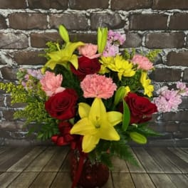 Bouquet of red roses, yellow lilies, and pink carnations in a red vase