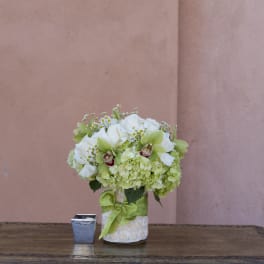 White and green floral arrangement in a decorated vase with a green ribbon