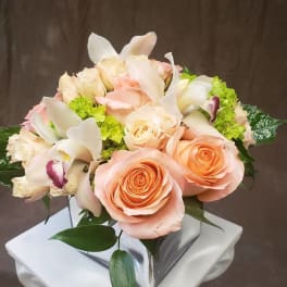 Peach roses and white orchids in a square glass vase
