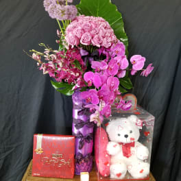 Pink roses and orchids arranged with a teddy bear and chocolates