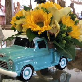 Sunflowers and pale yellow orchids arranged in a turquoise truck planter