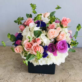 Mixed pink, white, and purple flower arrangement in a black box