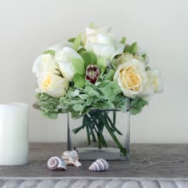 White roses in a square glass vase with green hydrangea and shells