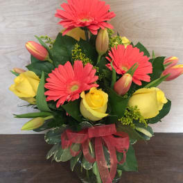 Bouquet of pink gerbera daisies and yellow roses in a glass vase with a red ribbon
