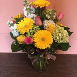 Bouquet of yellow gerbera daisies, pink roses, and white blooms in a glass vase